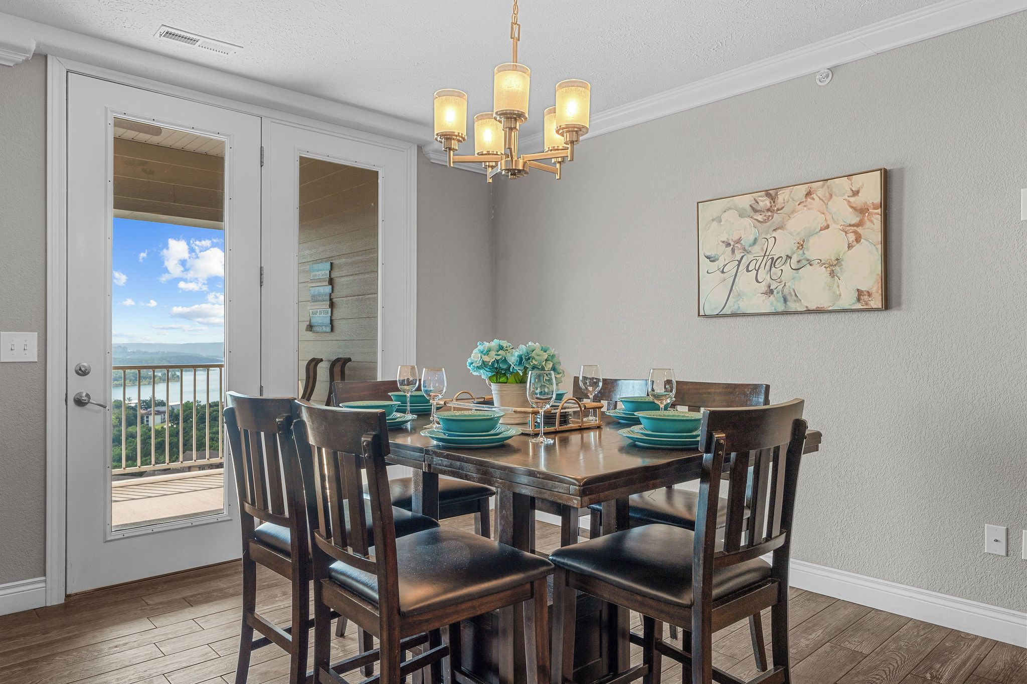 A dining area with a table set for four, wooden chairs, a chandelier, and a view through a glass door.