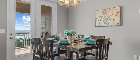 A dining area with a table set for four, wooden chairs, a chandelier, and a view through a glass door.