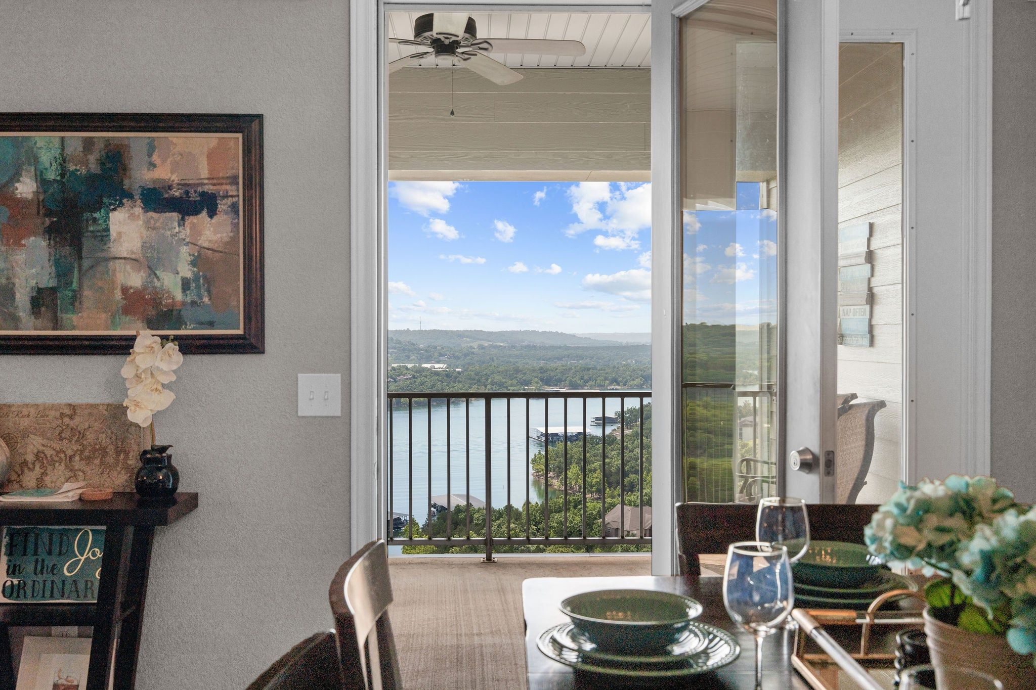 A dining area with a view of a lake and mountains, a ceiling fan, and a table set with plates and glasses.