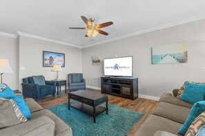 A living room with a ceiling fan, a flat-screen TV, and a sofa set.