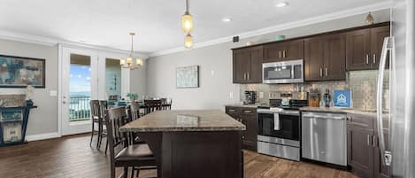 A modern kitchen with a central island, dark wooden cabinets, stainless steel appliances, and a dining area with a view.
