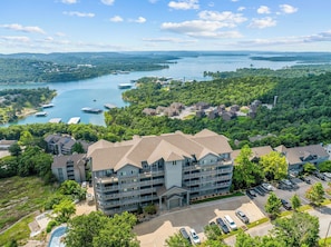A multi-story hotel with a central courtyard, surrounded by lush greenery and a body of water. - Luxury Condo with Lake Views, Free WiFi & Minutes from Silver Dollar City (Branson)