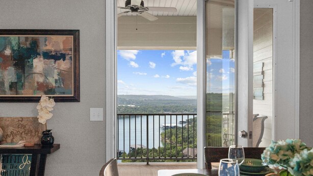 A dining area with a view of a lake and mountains, a ceiling fan, and a table set with plates and glasses. - Luxury Condo with Lake Views, Free WiFi & Minutes from Silver Dollar City (Branson)