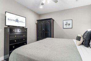 A bedroom with a bed, dresser, wardrobe, television, and artwork.