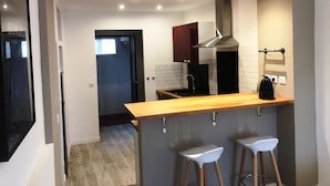 Una cucina moderna con piano di lavoro in legno, due sgabelli da bar bianchi, una cappa aspirante in acciaio inossidabile e uno schienale nero.