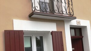 Un edificio con un balcone, una finestra con persiane rosse e una porta con un numero.