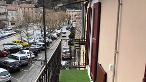 Un balcone con erba sintetica verde, ringhiera in metallo e vista su un parcheggio con diverse automobili.