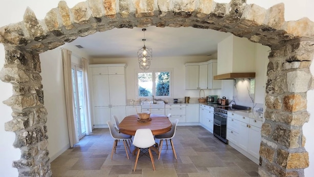 Una cucina con un arco in pietra, mobili bianchi, un tavolo da pranzo in legno con sedie e una lampada a sospensione.