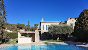 Una villa in pietra con piscina, un ponte in pietra e un grande ulivo.
