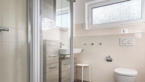 Un baño moderno con cabina de ducha de vidrio, tocador de madera, un taburete pequeño y un inodoro.