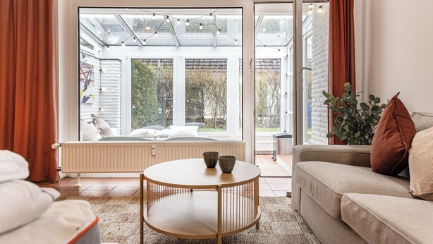 Una sala de estar con un sofá, una mesa redonda y vistas a una zona de estar exterior a través de un ventanal.