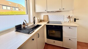 Una cocina moderna con ventana, armarios blancos, horno negro y pileta.