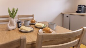 Una mesa de madera con platos de comida, un florero con flores y una cafetera.