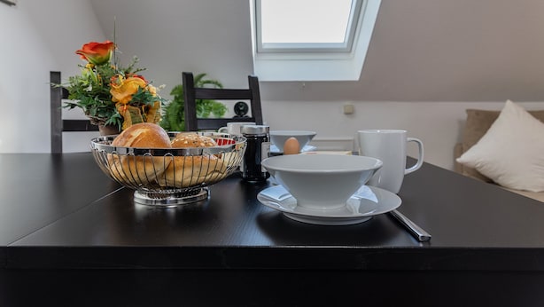 Un desayuno con pan, flores y una taza de café sobre una mesa negra.