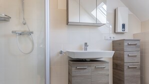 Un baño moderno con cabina de ducha de vidrio, un lavamanos blanco y muebles de madera.