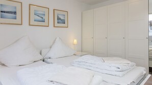 Habitación de hotel con dos camas, ropa de cama blanca, una mesita de noche con lámpara y un armario con espejo.