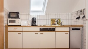 Una cocina con armarios blancos, microondas, cafetera y lavavajillas.