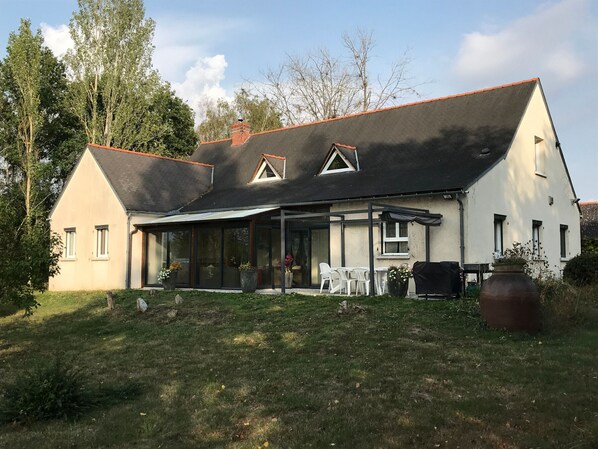 Une maison à deux étages dotée d’un patio couvert, de grandes fenêtres et d’un jardin.