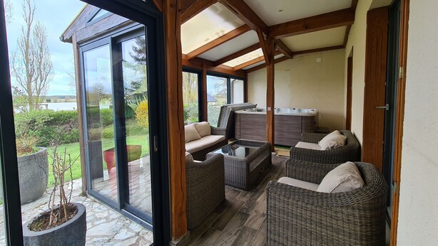 Een zonnig terras met rieten meubilair, een jacuzzi en uitzicht op de omgeving.