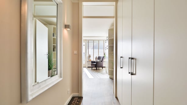 A hallway with a mirrored wall, a door leading to a room with a chair and a small table, and a doormat with "Lounge Club" text. - The Sunny Side - Westerland (Westerland)