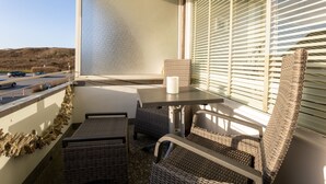 A balcony with wicker furniture, a table, and a view of a parking lot and hills. - The Sunny Side - Westerland (Westerland)