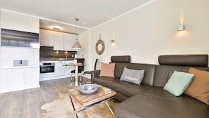 A modern living room with a leather sofa, a glass coffee table, and a dining area with a kitchen in the background. - The Sunny Side - Westerland (Westerland)