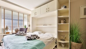 A modern bedroom with a bed, built-in shelving, a potted plant, and a window with blinds. - The Sunny Side - Westerland (Westerland)