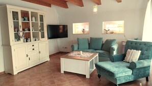 A living room with a wooden ceiling, a television, a cabinet with glass doors, a blue sofa, and a coffee table.