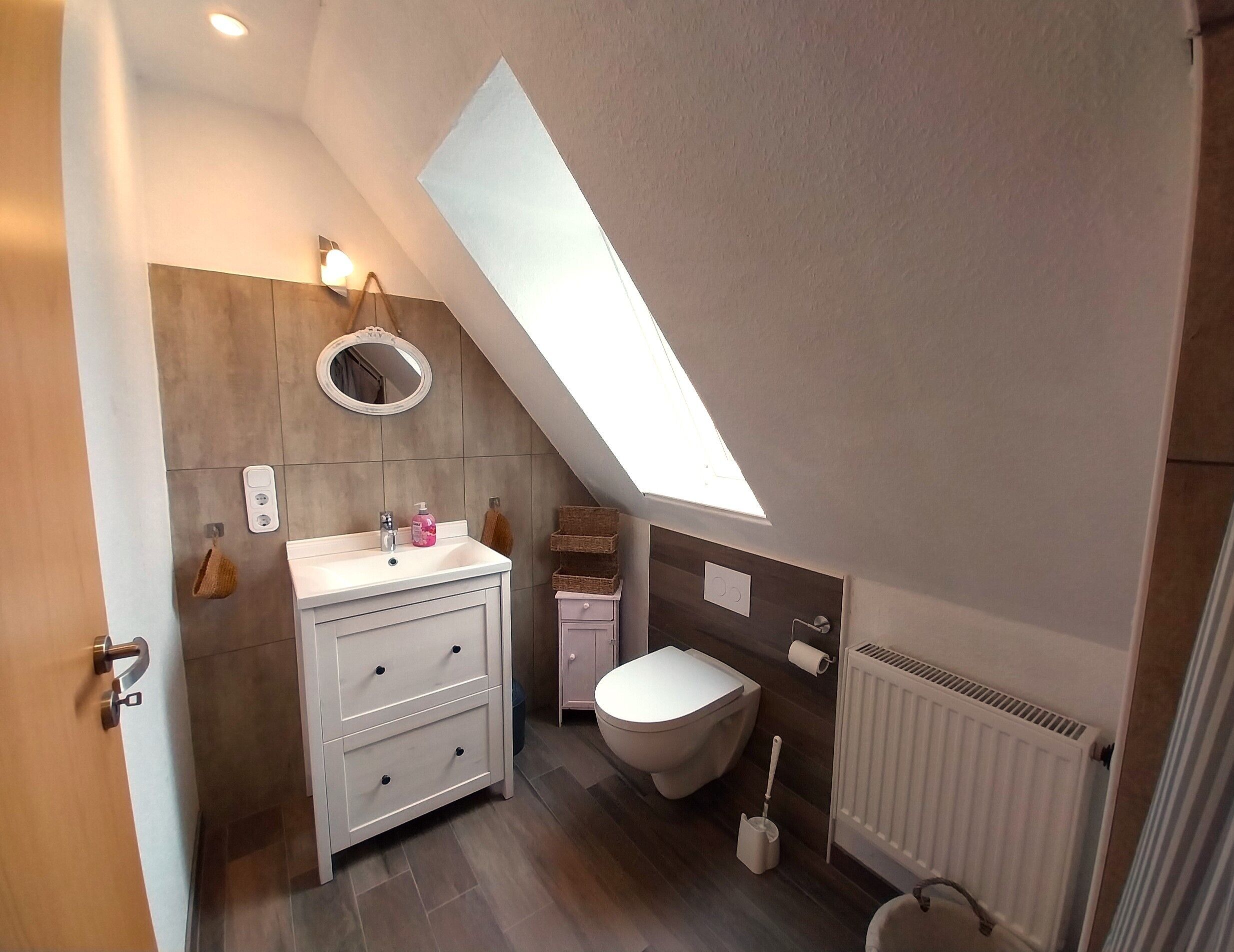 A modern bathroom with a skylight, a white vanity, a toilet, and a radiator.