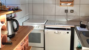 Ett kompakt kök med vita kakelväggar, träskåp, en diskmaskin från Bosch, en spis och en vattenkokare.