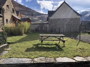 En rustik byggnad med en fasad av sten, ett träbord för picknick och en stenmur som omger området.