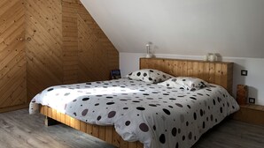 Ett sovrum med ett lutande tak av trä, en säng med ett sängöverkast i prickigt mönster och ett sängbord med en lampa och ljus.