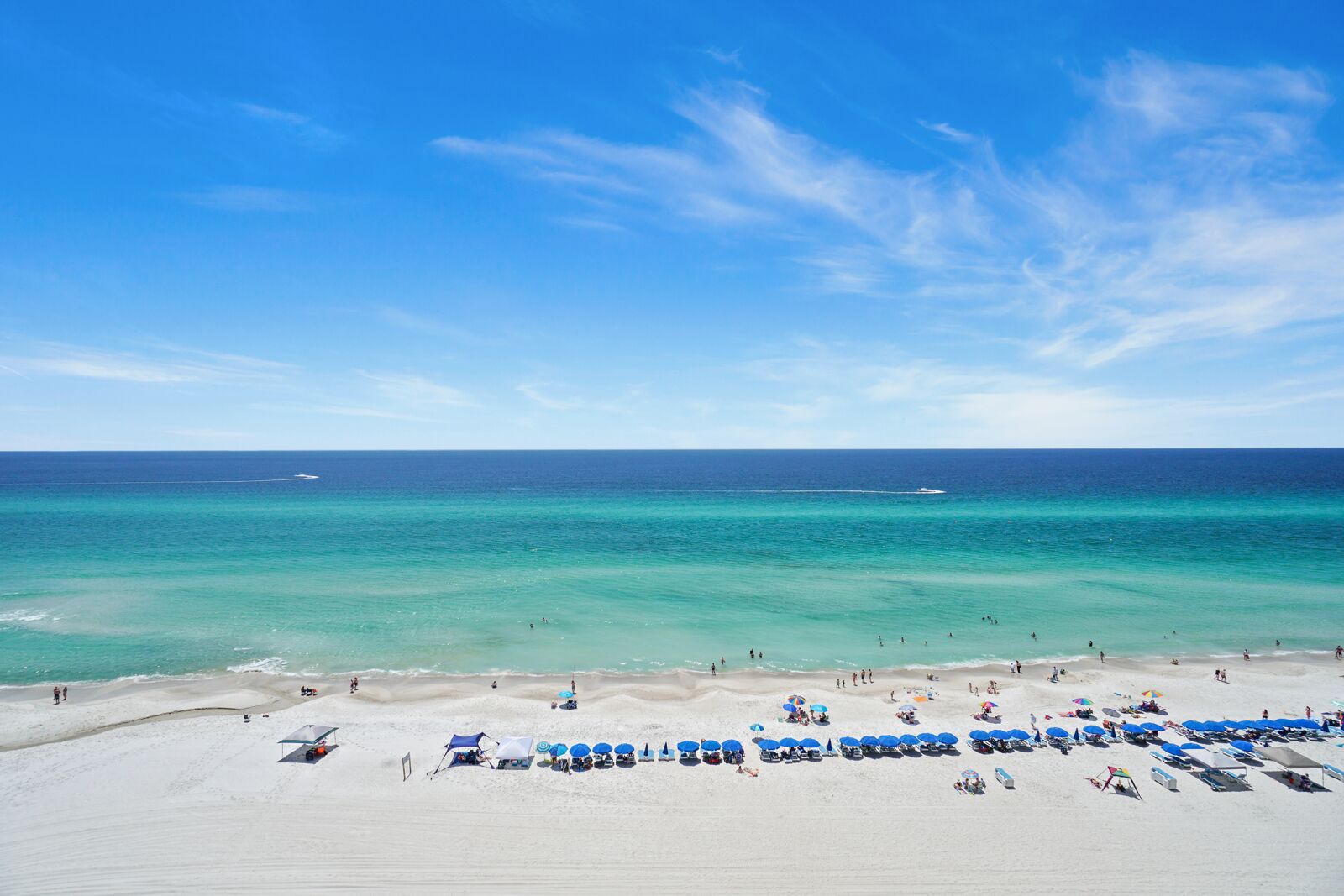A beach with clear turquoise waters, a sandy shore, and several blue umbrellas and beach chairs.