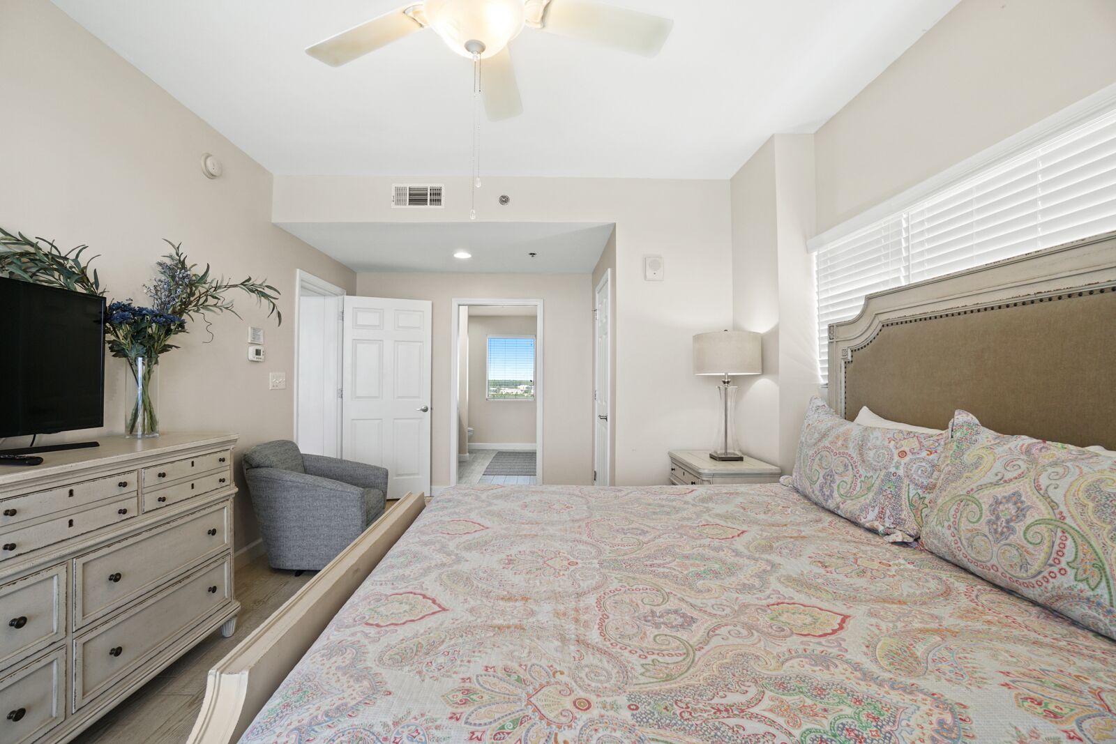 A bedroom with a bed, dresser, TV, and a ceiling fan.