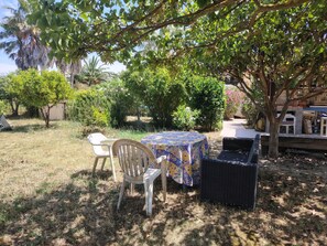 An outdoor patio with a round table covered by a patterned tablecloth, surrounded by wicker furniture and a white plastic chair. - APARTMENT BETWEEN THE SEA AND THE COUNTRYSIDE UNDER THE SUN OF THE FRENCH RIVIERA (LA CRAU)