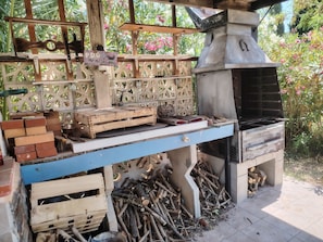 An outdoor cooking area with a grill, wooden crates, and a sign that reads 'P.D.G PRO DES GRILLADES'.