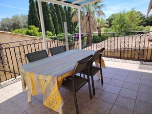 An outdoor patio with a table and chairs, surrounded by a metal fence and greenery.