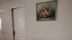 En vit soffa med röda kuddar, en tavla med blommor på väggen och en vit dörr i bakgrunden.