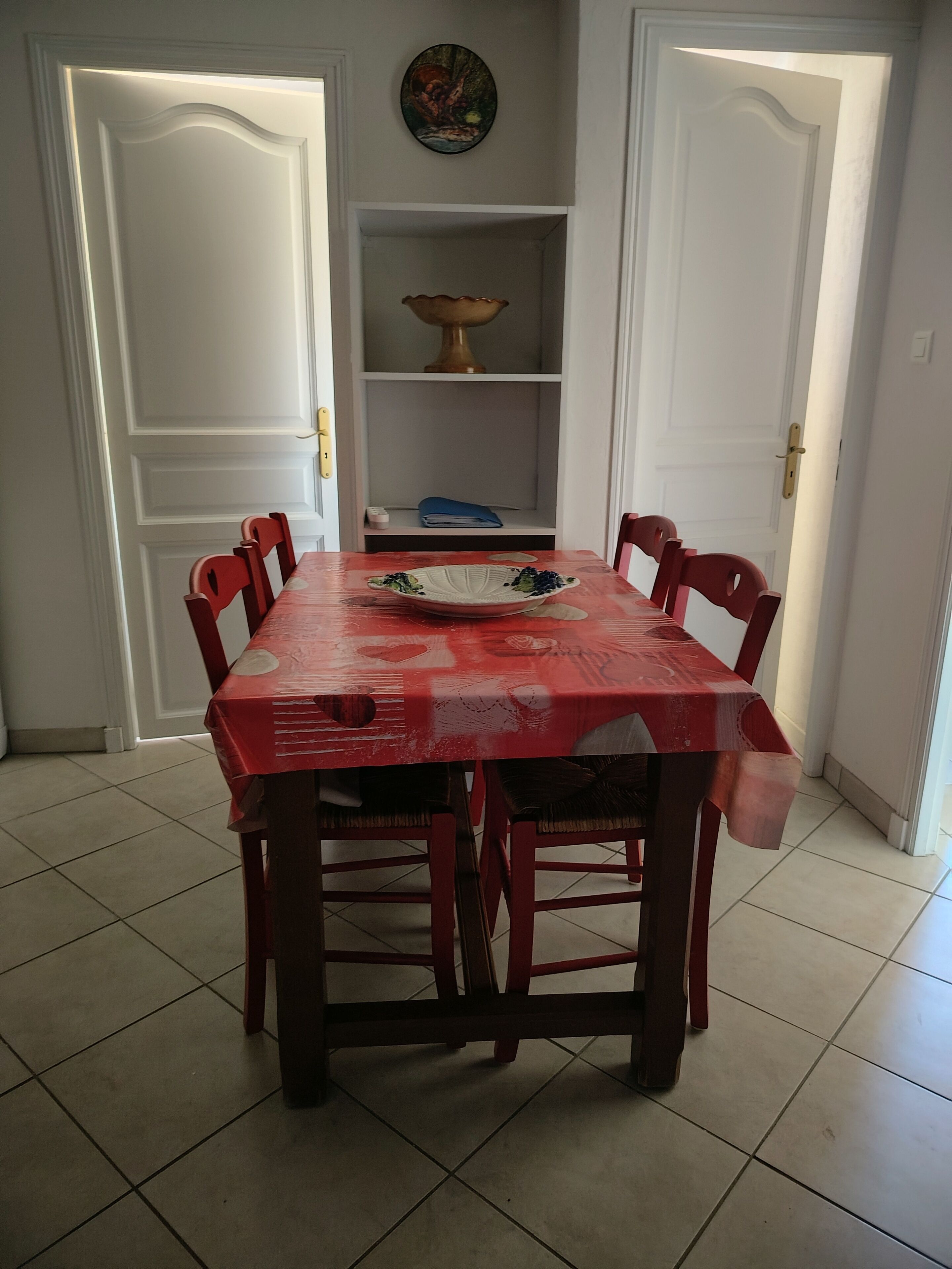 Una mesa de comedor con sillas, un cuenco decorativo y una estantería con una lámpara y objetos doblados.