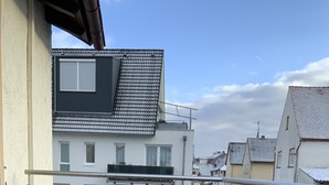 Un balcón con una mesa y sillas, vista a edificios vecinos y cielo despejado.
