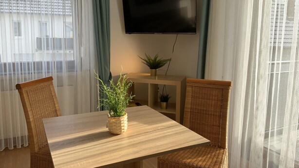 Un comedor con mesa de madera, sillas de mimbre y una planta en maceta.