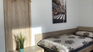 Un dormitorio con una cama, un armario de madera, un armario colgado, un cuadro en la pared y una planta en maceta.