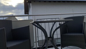 Un balcón con mobiliario de mimbre y barandilla metálica.