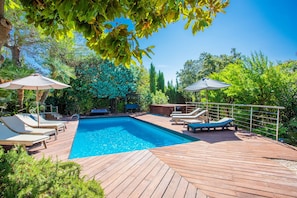Une terrasse en bois avec une piscine, des chaises longues et des parasols.