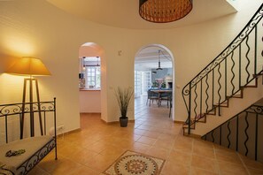 A staircase with ornate metal railings, a potted plant, and a lamp in a hallway leading to a dining area. - VILLA JUSTINE VI4239 By Riviera Holiday Homes (Mandelieu-la-Napoule)
