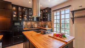 Une cuisine moderne avec des meubles de couleur sombre, un plan de travail en bois et une grande fenêtre qui laisse entrer la lumière naturelle.