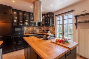 Une cuisine moderne avec des meubles de couleur sombre, un plan de travail en bois et une grande fenêtre qui laisse entrer la lumière naturelle.