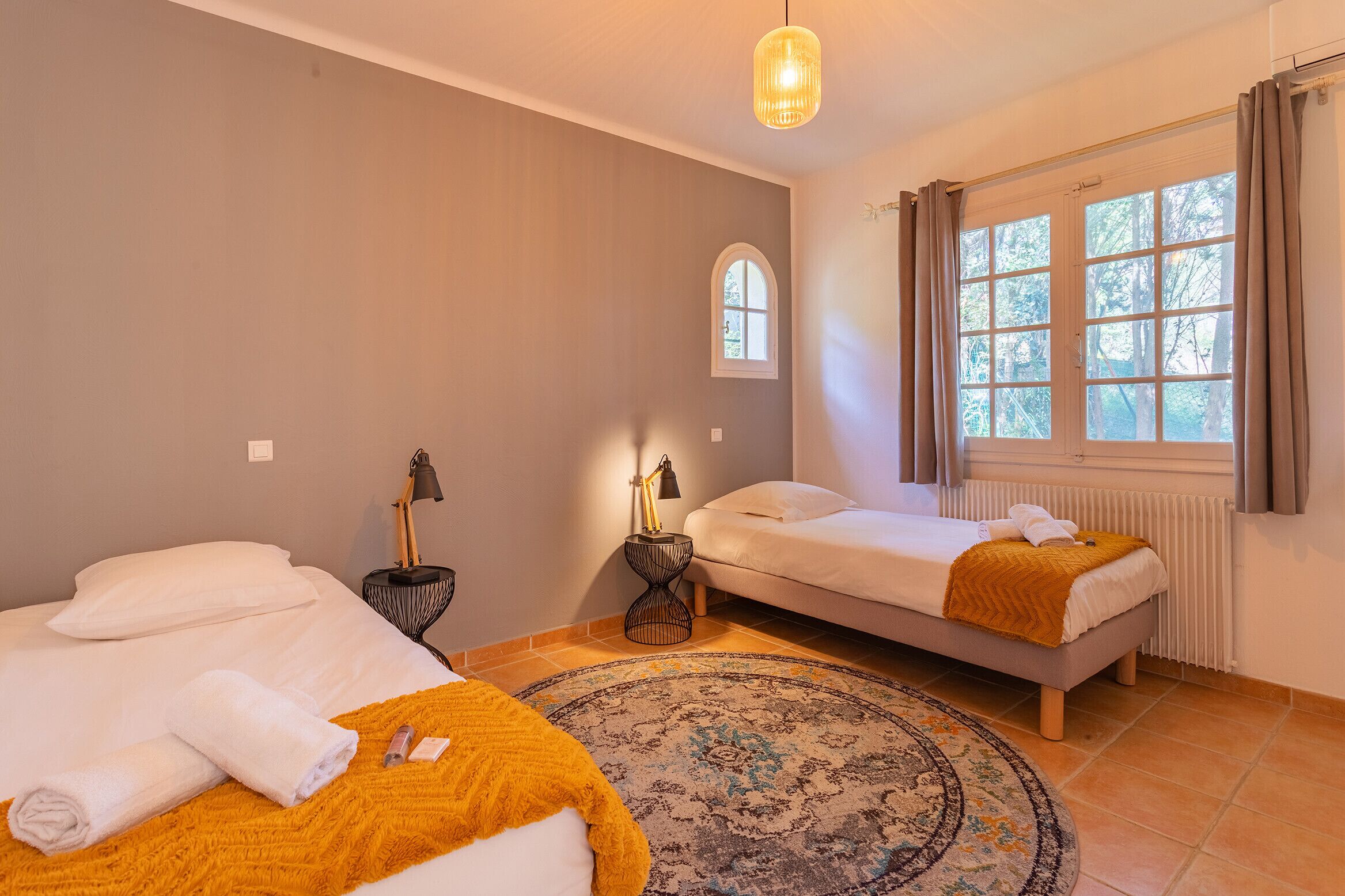 A bedroom with two beds, a window with curtains, a lamp, and a rug.