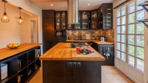 A modern kitchen with a central island, dark cabinetry, and a large window providing natural light. - VILLA JUSTINE VI4239 By Riviera Holiday Homes (Mandelieu-la-Napoule)