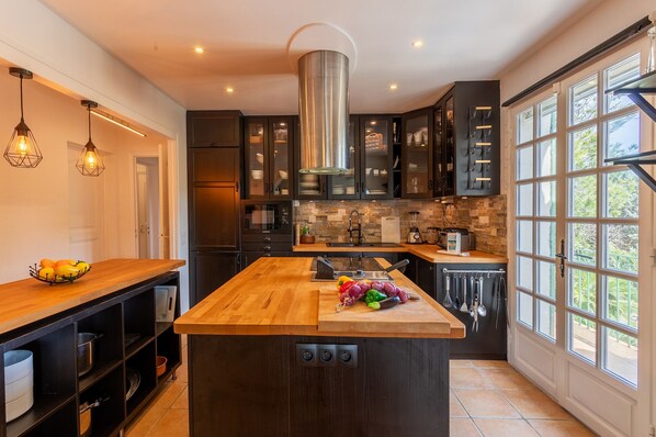 Une cuisine moderne dotée d’un îlot central, de meubles de rangement aux couleurs sombres et d’une grande fenêtre qui laisse entrer la lumière naturelle.